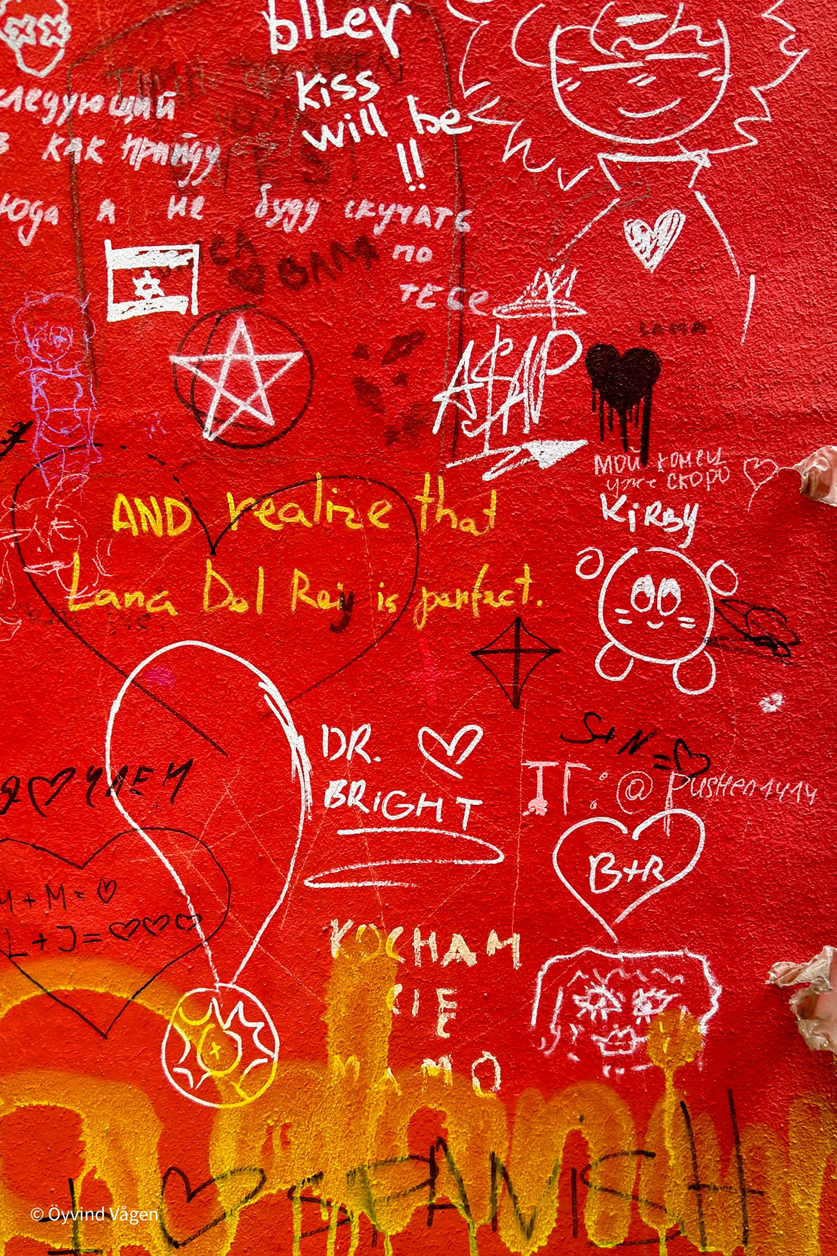 Röd vägg med graffiti och texter.