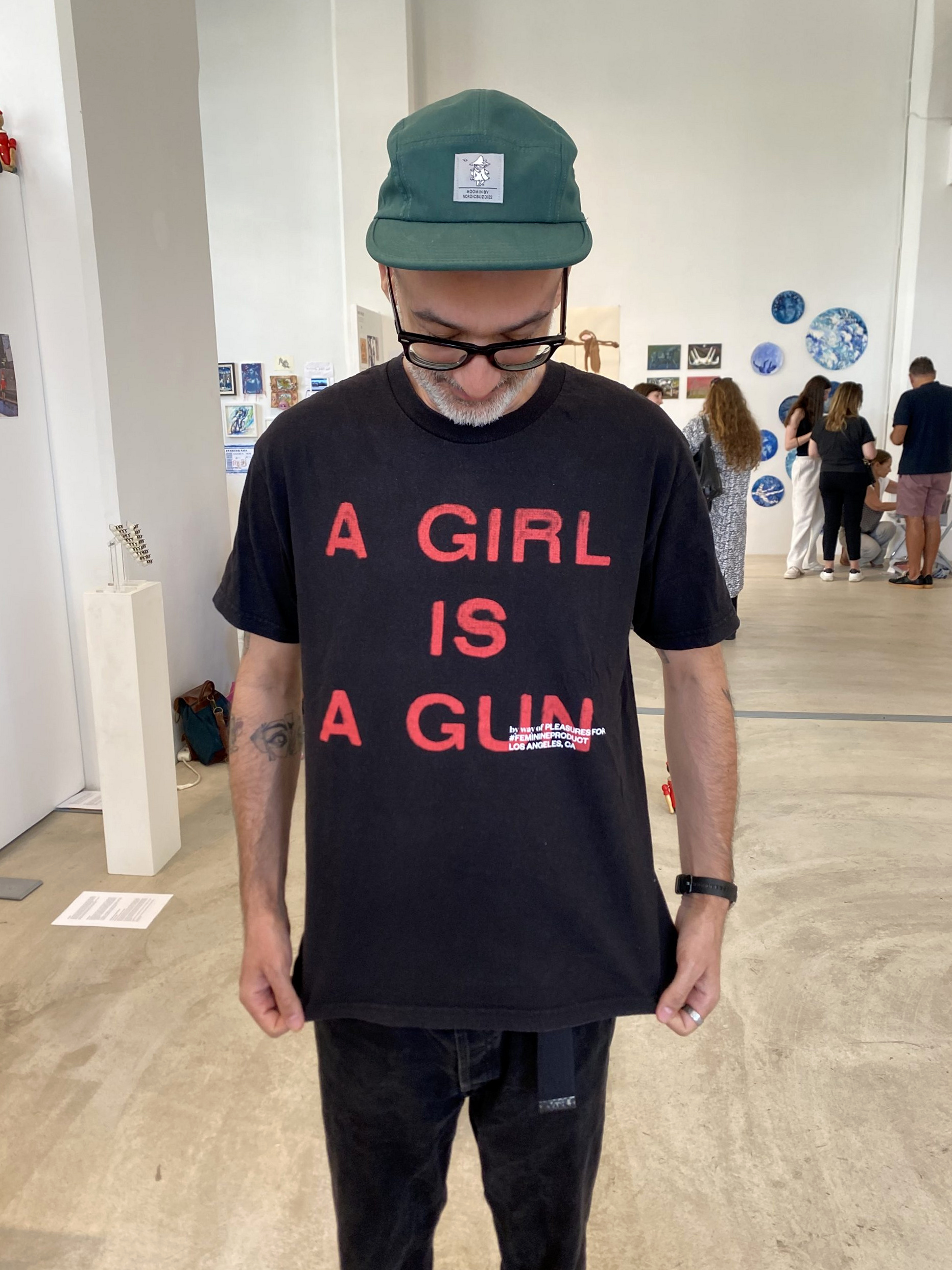 Besökare i grön keps och svart tröja med texten A GIRL IS A GUN.