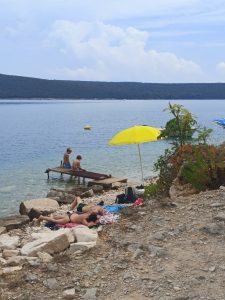 A yellow parasol and swimmers beside a rocky shore