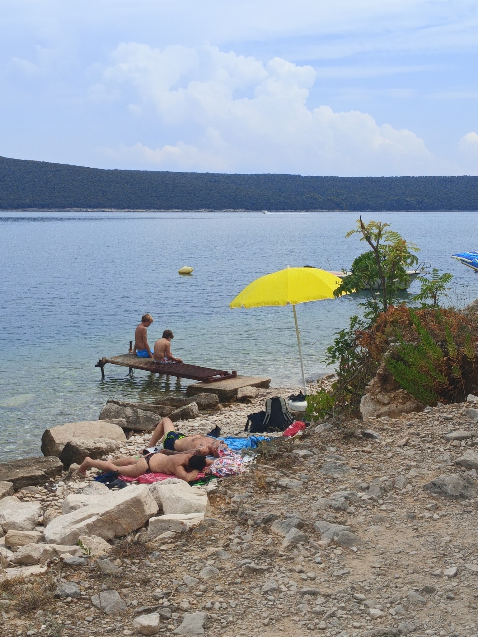 A yellow parasol and swimmers beside a rocky shore