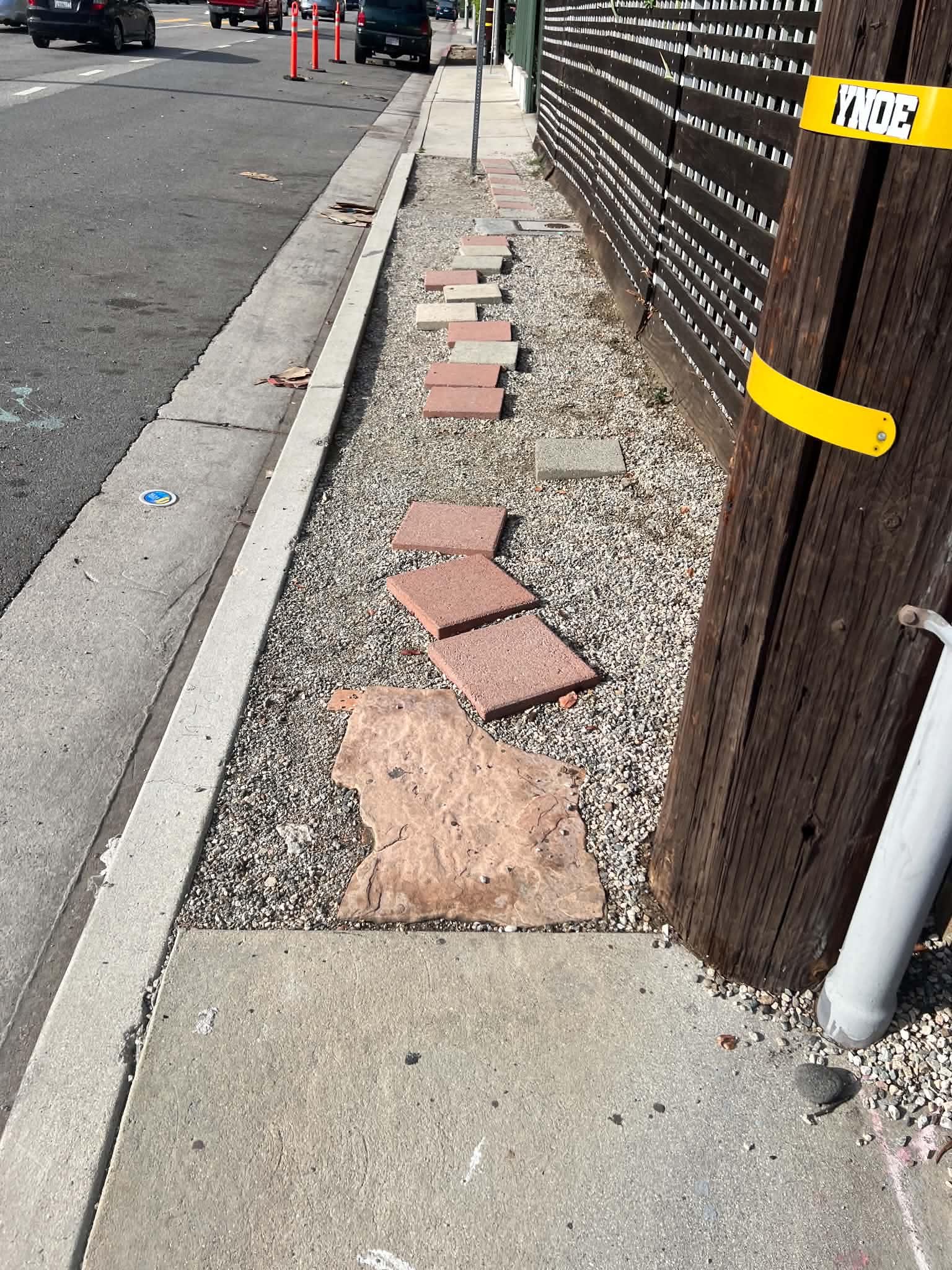 Trasig beläggning och tegelstenar längs en smal trottoar.